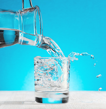 Water pouring into a glass on blue background